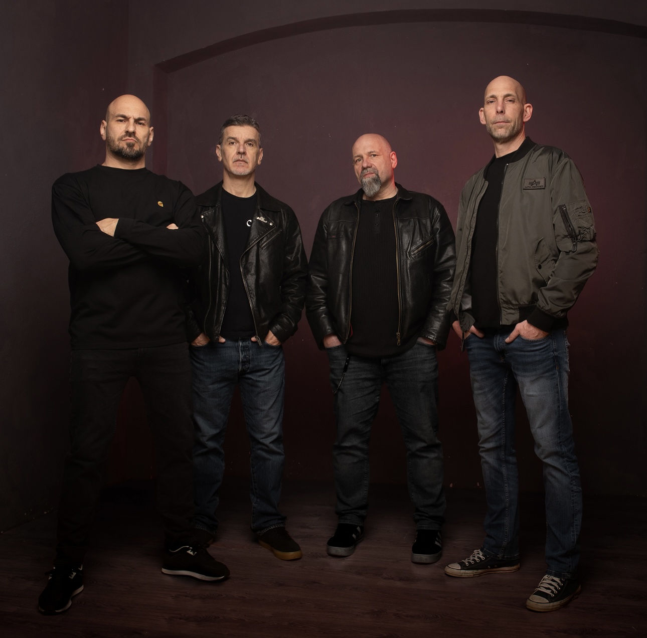 Magma Rise band photo — four members standing against a dark red backdrop
