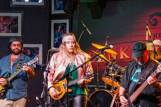 Fox Maple performing live with her band on a small club stage, guitarist and bassist either side of her