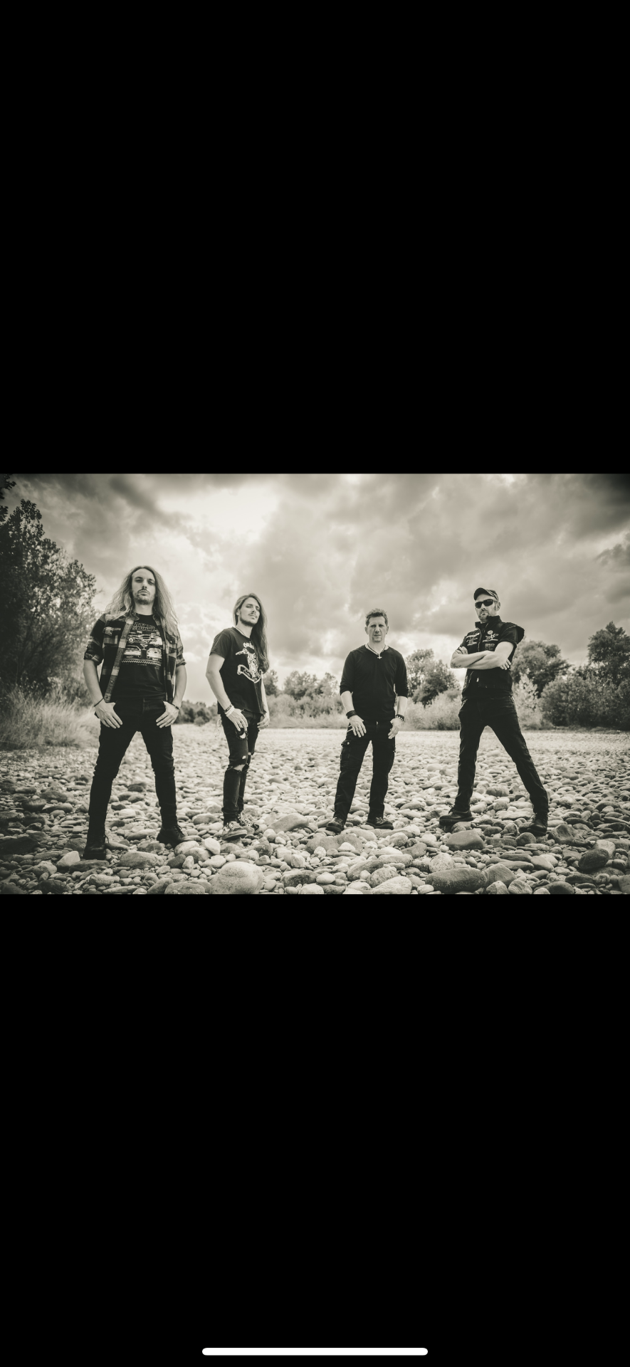 Hellgeist band promo photo — four members standing on a riverbed under a cloudy sky