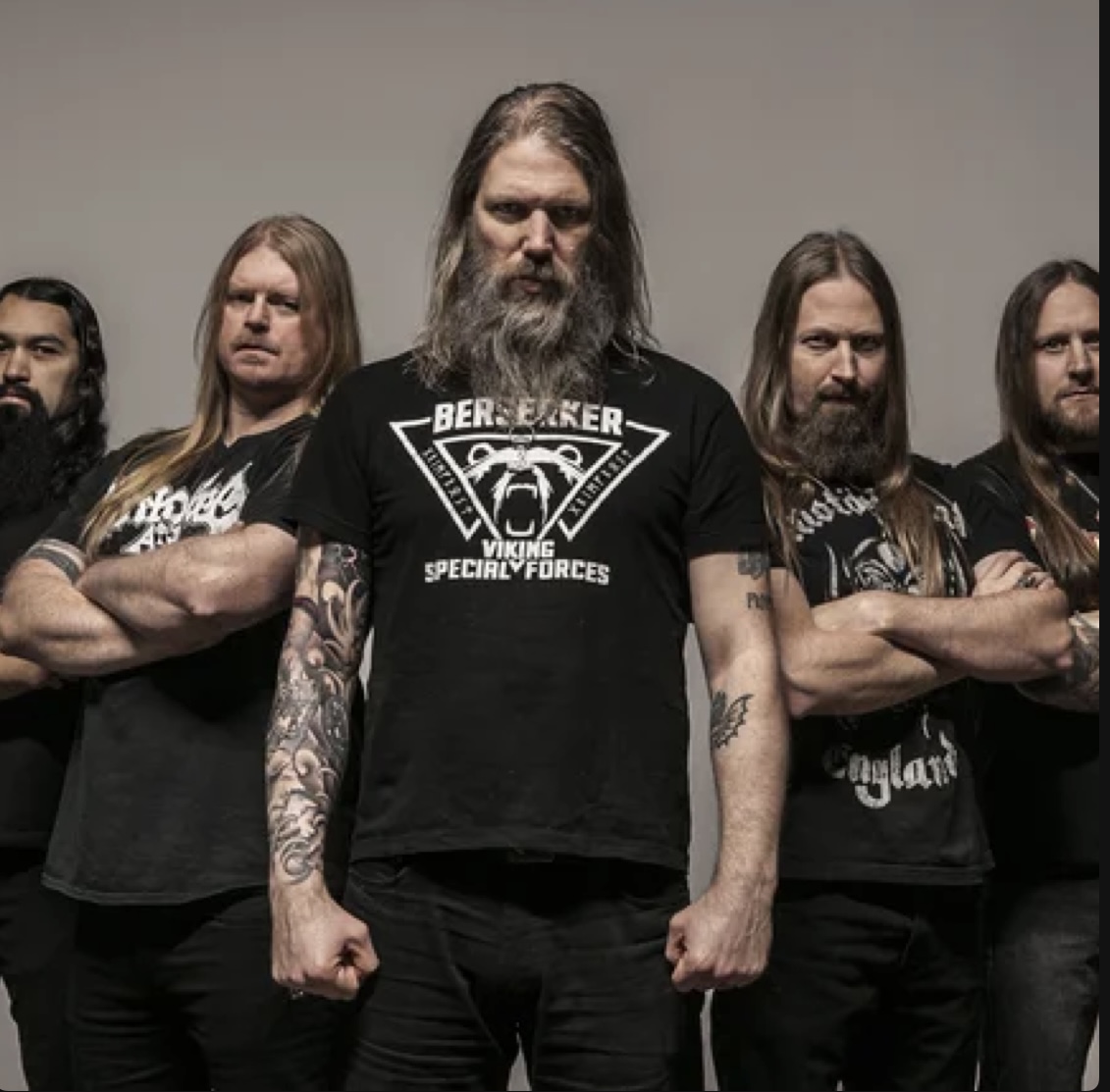Amon Amarth band photo — the five Swedish Viking metal musicians standing with arms crossed against a grey backdrop