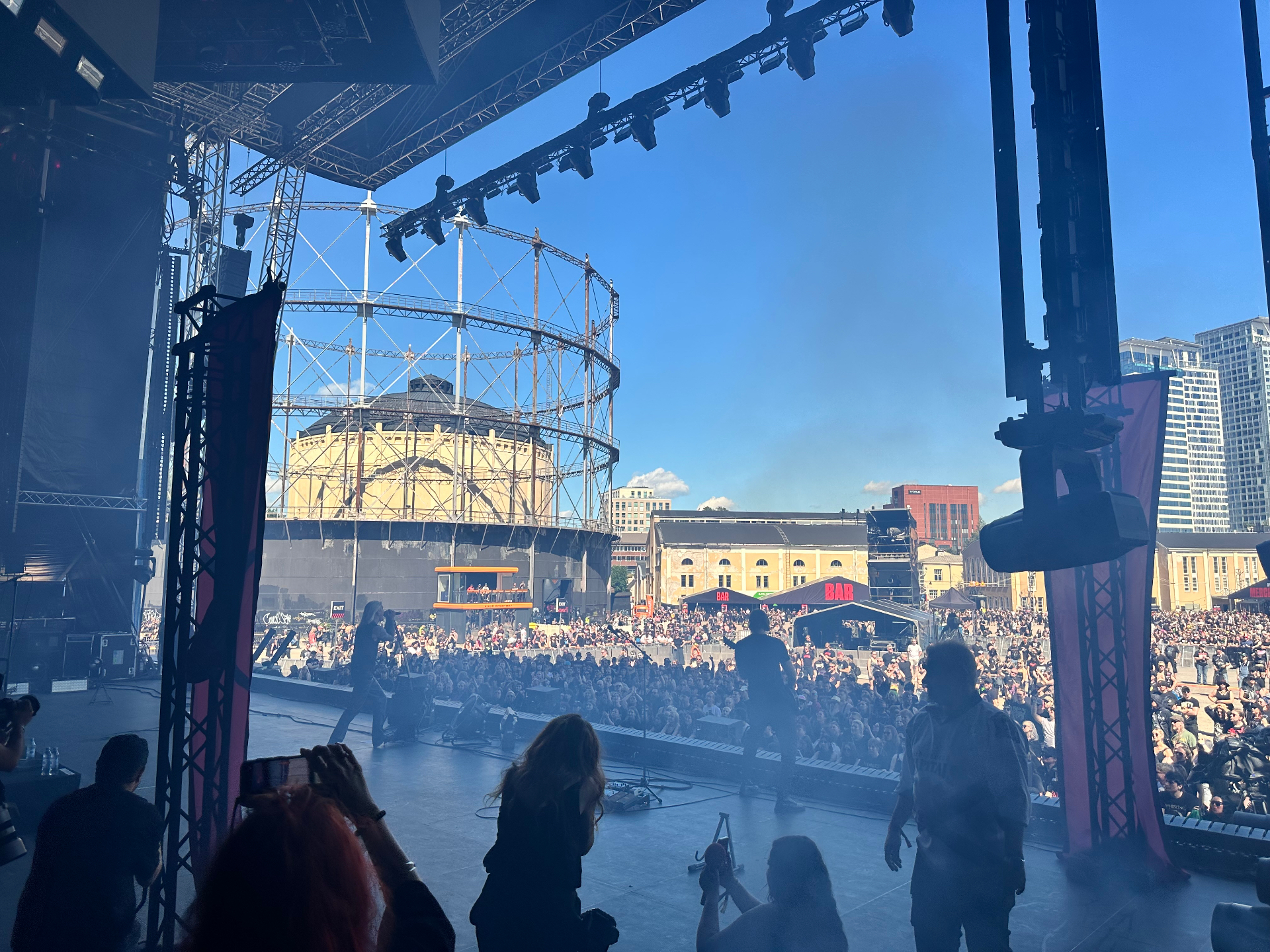 Day 2 — Side-stage with the media tour watching Hokka command a massive crowd at Suvilahti. Backstage side-stage view of Hokka performing at Tuska Festival 2026 with the Suvilahti gasometer in the background