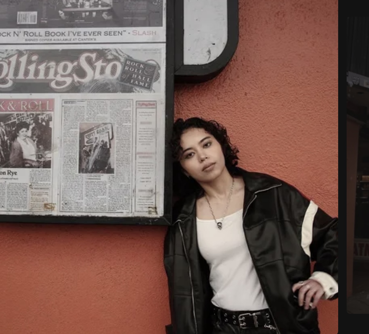 XANA photographed outside against a coral wall in a black leather jacket