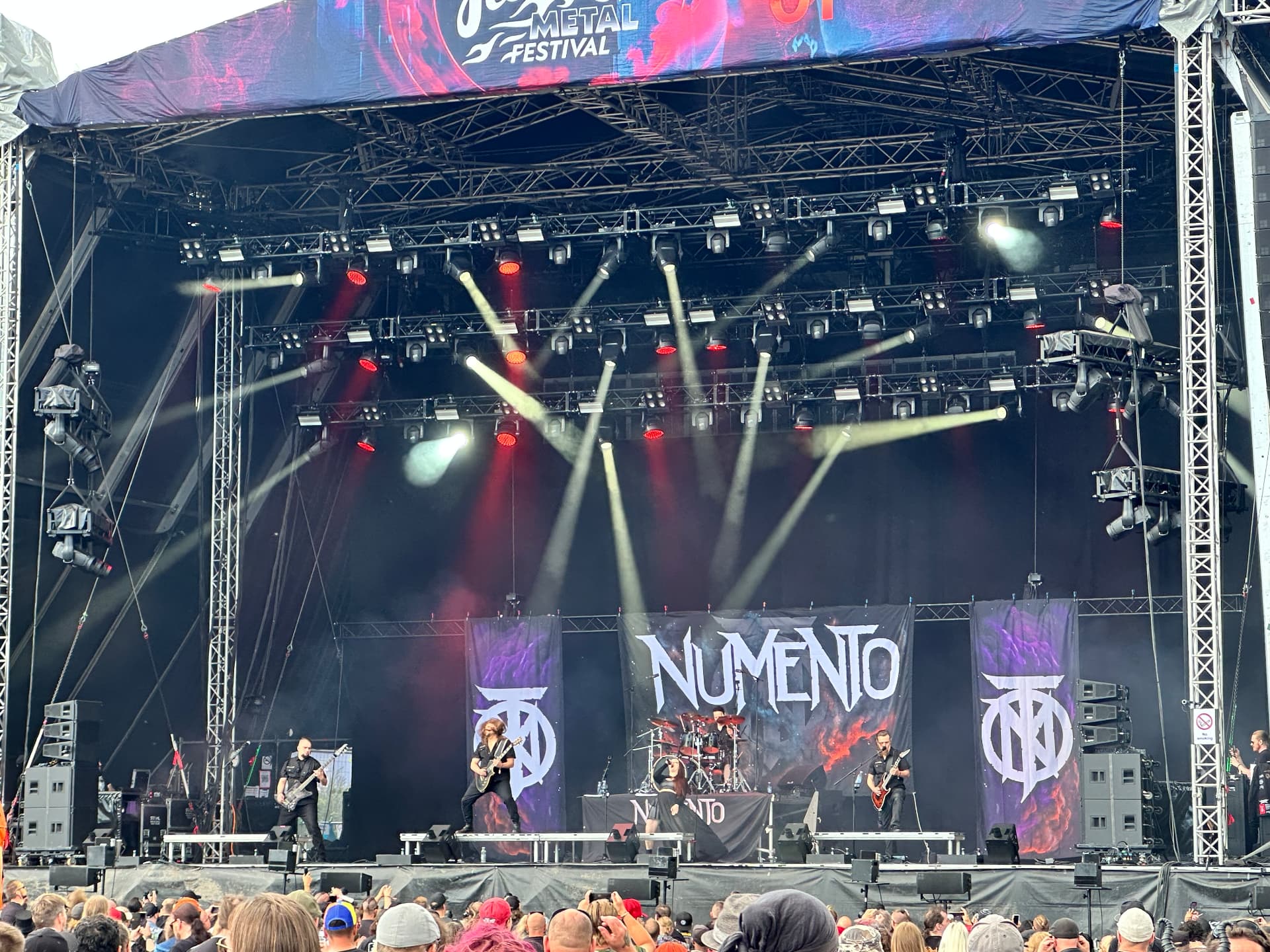Numento — banners, beams and big choruses. Numento performing at Hellsinki Metal Festival 2026 with banners and a full light show on the outdoor stage