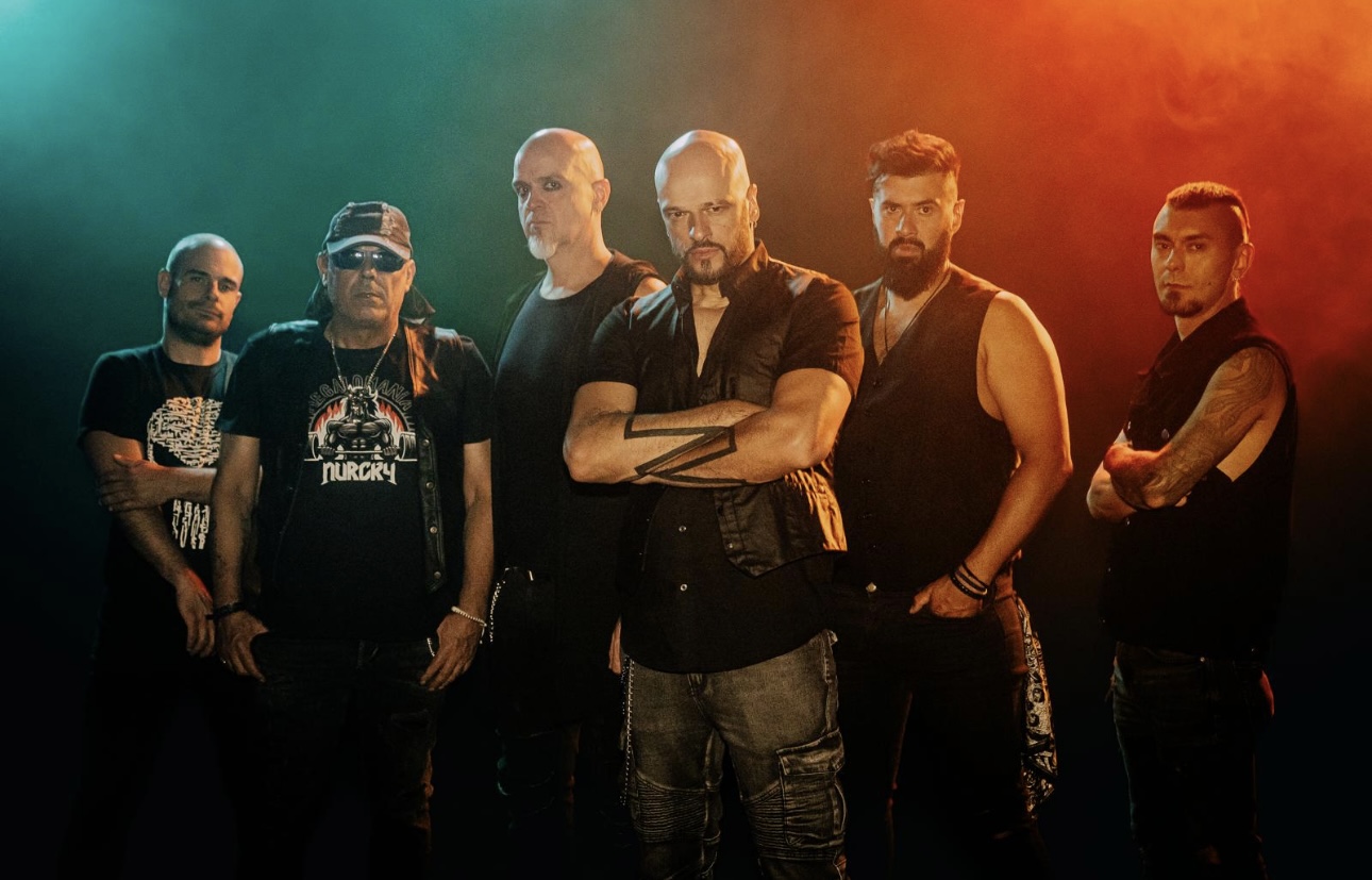The six members of Spanish heavy metal band NURCRY standing together in black stage clothing under teal and orange lighting