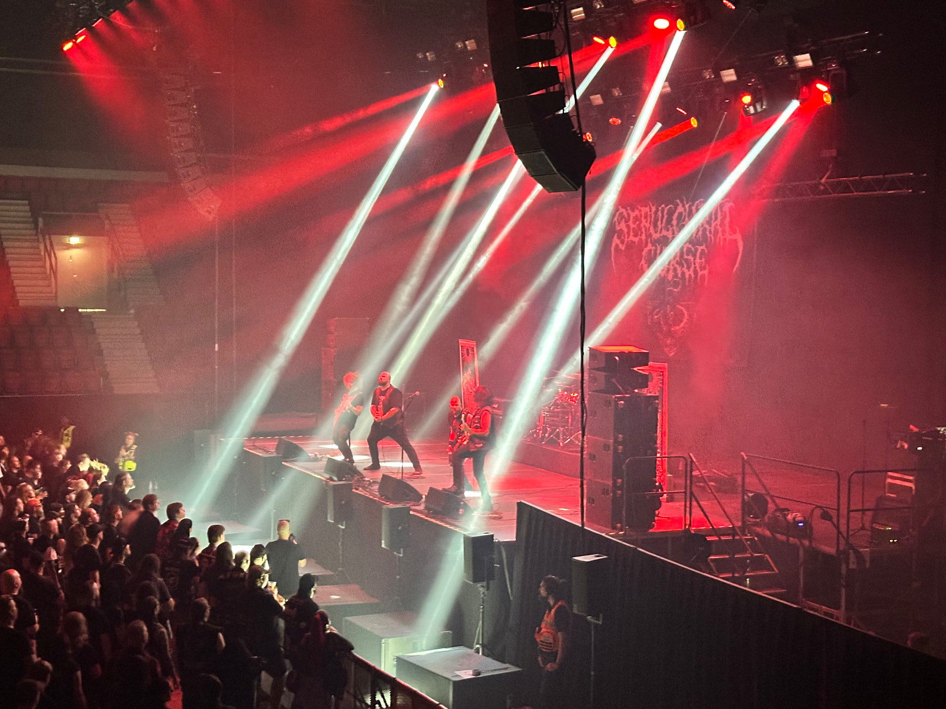 Sepulchral Curse — death metal indoors on Hellsinki-03. Sepulchral Curse performing indoors at Hellsinki Metal Festival 2026 in red light with white beams cutting through smoke