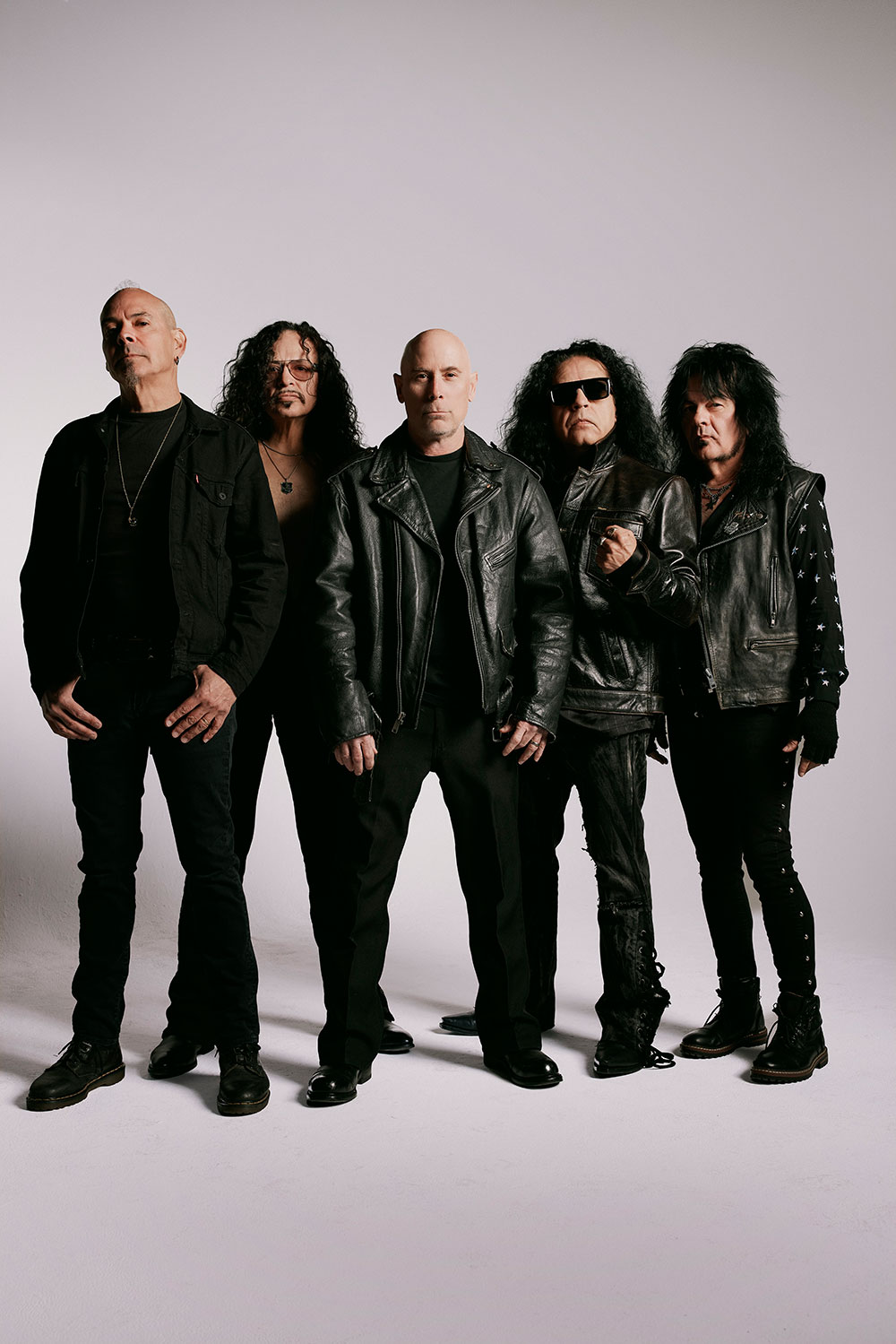 Armored Saint band photo — five members in black leather against a light studio backdrop