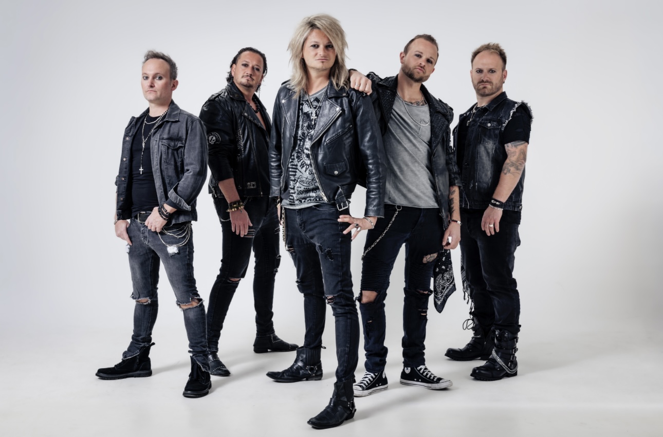 KISSIN' DYNAMITE band photo — five members in leather and denim against a light studio backdrop