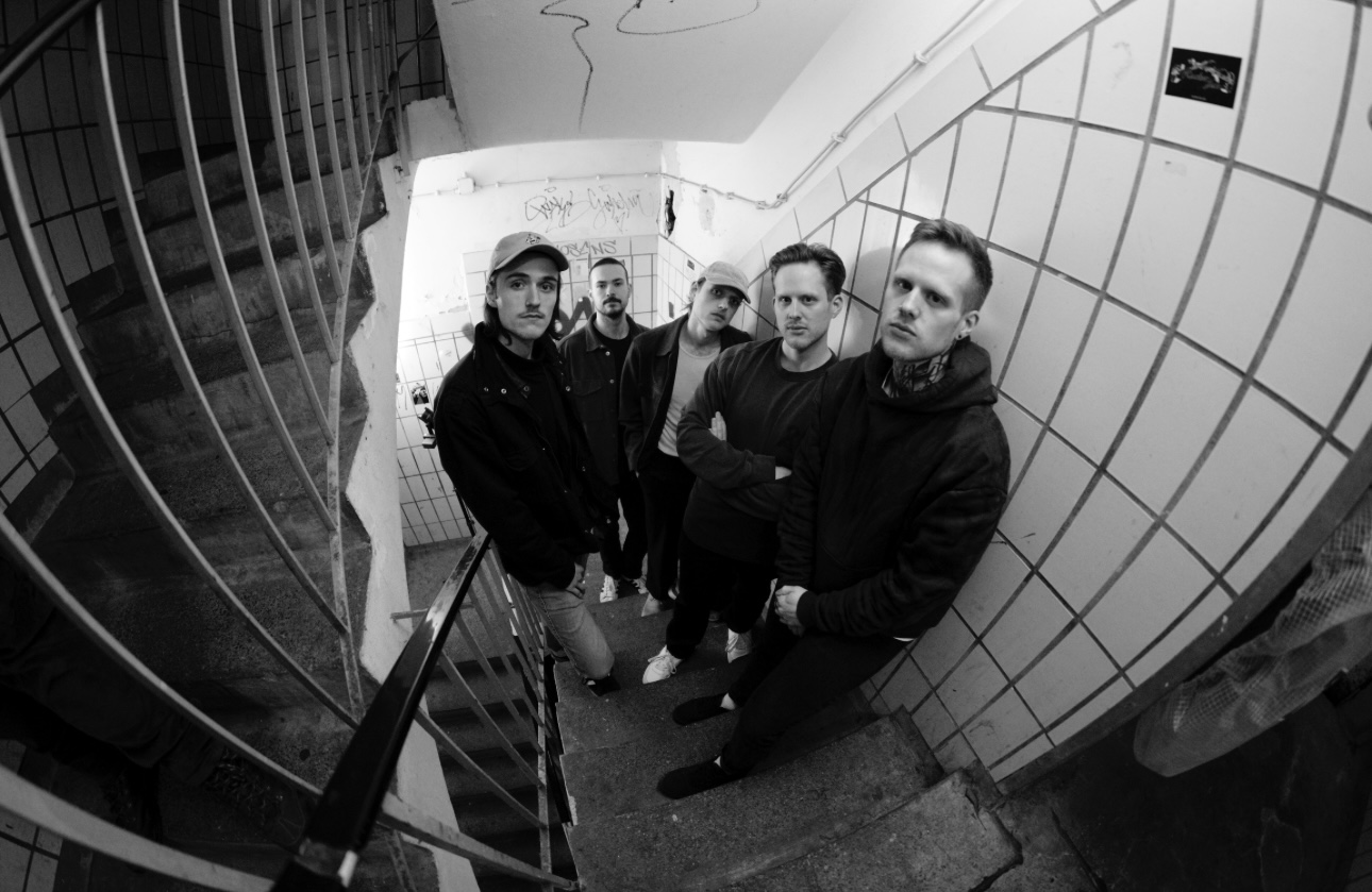 Black and white photo of Paradise in Fear: five band members standing in a tiled stairwell shot with a fisheye lens