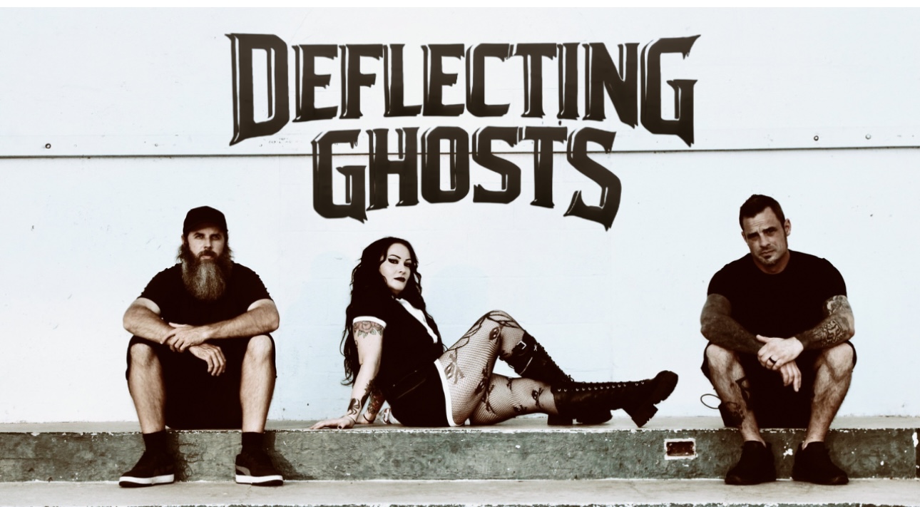 Deflecting Ghosts band photo — the three-piece alternative metal band from Hutchinson, Kansas seated in front of the band name on a white wall